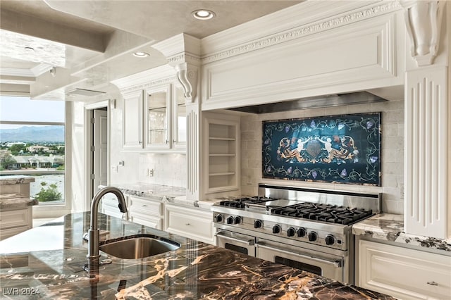 kitchen featuring double oven range, sink, ornamental molding, light stone countertops, and white cabinetry