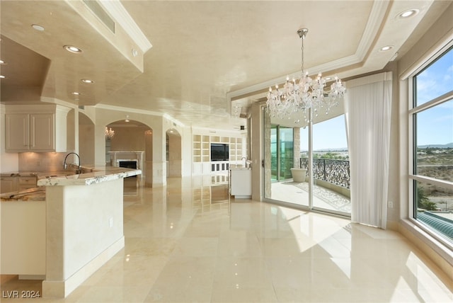 kitchen featuring a notable chandelier, tasteful backsplash, ornamental molding, light stone countertops, and pendant lighting