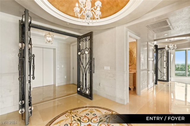 entryway with ornamental molding, a tray ceiling, and an inviting chandelier