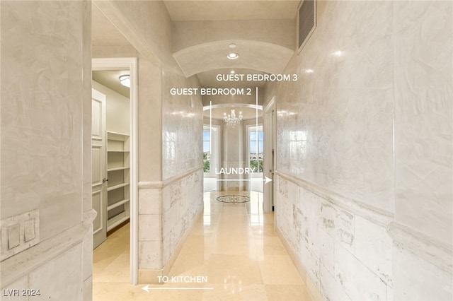 hall with tile walls and an inviting chandelier