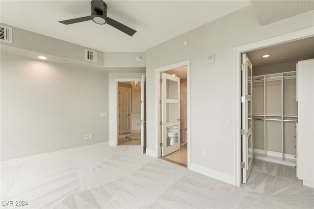 unfurnished bedroom with a closet, a spacious closet, connected bathroom, light colored carpet, and ceiling fan