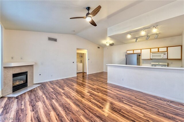 unfurnished living room with a tile fireplace, ceiling fan, dark wood-type flooring, washer / clothes dryer, and vaulted ceiling