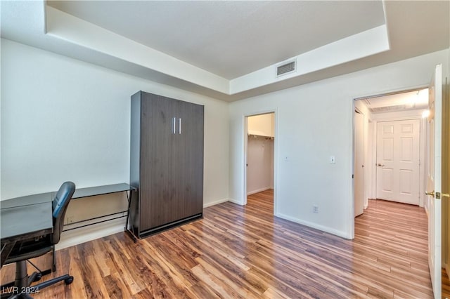 office with a tray ceiling, wood finished floors, and visible vents