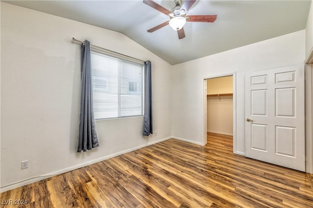 unfurnished bedroom featuring a walk in closet, lofted ceiling, a closet, wood finished floors, and baseboards