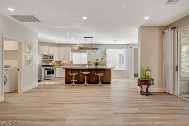 kitchen with stainless steel appliances, a kitchen island, light wood-type flooring, white cabinetry, and a kitchen breakfast bar