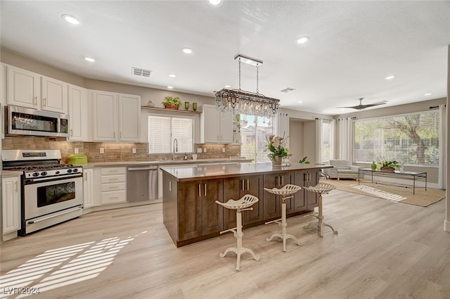 kitchen with appliances with stainless steel finishes, a kitchen bar, hanging light fixtures, light hardwood / wood-style floors, and a center island