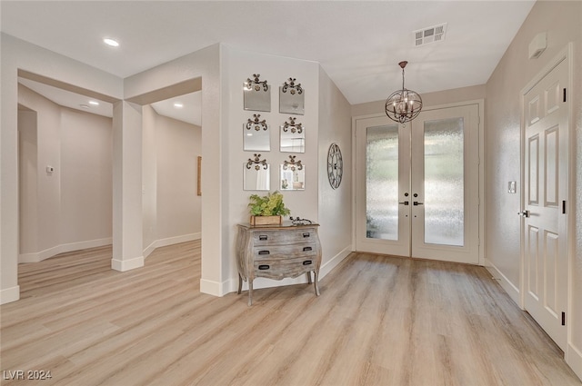 foyer entrance with light hardwood / wood-style floors, french doors, and a notable chandelier