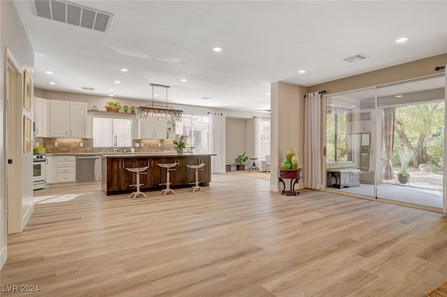 kitchen with a kitchen island, stainless steel dishwasher, hanging light fixtures, and light hardwood / wood-style floors