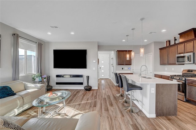 kitchen with sink, appliances with stainless steel finishes, decorative light fixtures, an island with sink, and light wood-type flooring