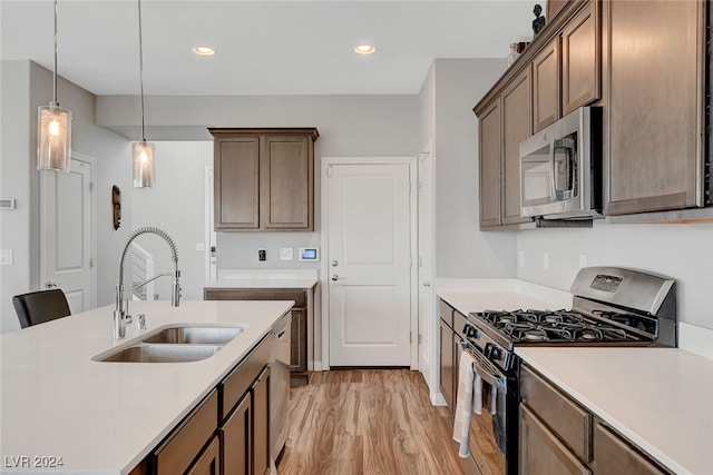 kitchen with decorative light fixtures, light wood-type flooring, sink, and stainless steel appliances