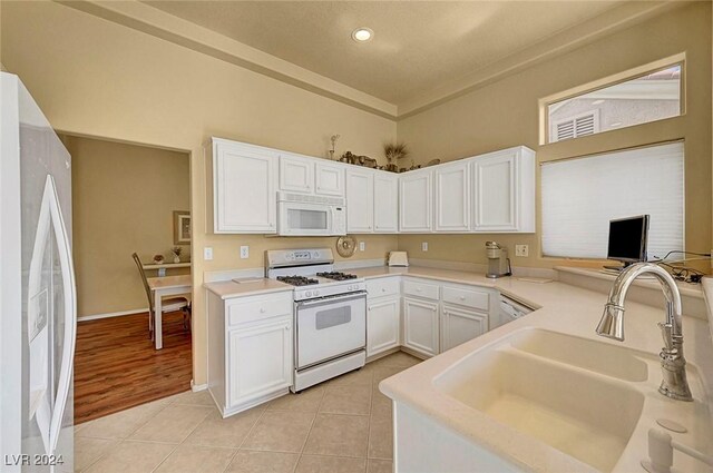 kitchen featuring white cabinetry, sink, kitchen peninsula, white appliances, and light tile patterned flooring