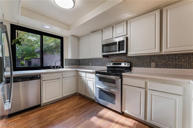 kitchen with stainless steel appliances, white cabinets, sink, tasteful backsplash, and light hardwood / wood-style flooring