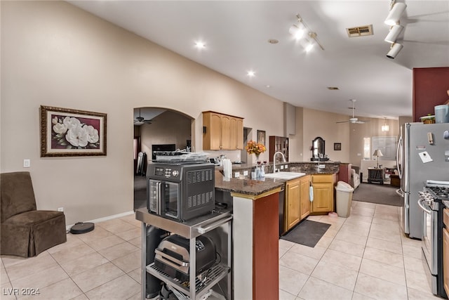 kitchen featuring lofted ceiling, dark stone counters, sink, light tile patterned floors, and stainless steel gas range