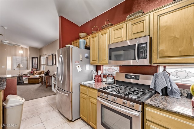 kitchen with appliances with stainless steel finishes, lofted ceiling, light tile patterned floors, and stone counters