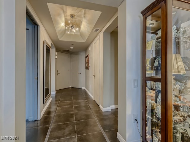 hallway featuring dark tile patterned flooring, a tray ceiling, and a notable chandelier