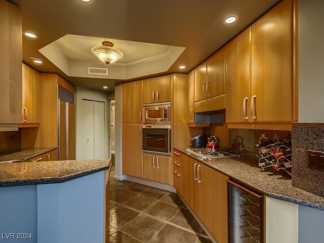 kitchen with wine cooler, dark stone counters, built in appliances, and a raised ceiling