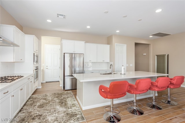 kitchen featuring stainless steel appliances, white cabinets, sink, an island with sink, and a kitchen breakfast bar