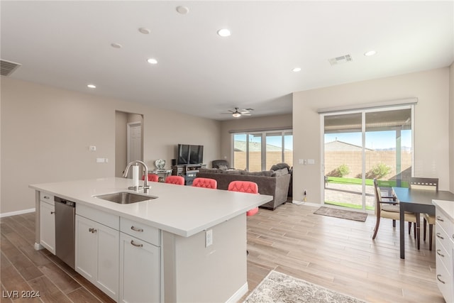 kitchen with white cabinetry, sink, an island with sink, stainless steel dishwasher, and light wood-type flooring