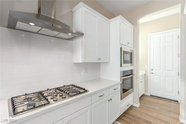 10254 Baronia St, Las Vegas, NV 89141 - kitchen featuring wall chimney exhaust hood, stainless steel appliances, light wood-style floors, light countertops, and white cabinets