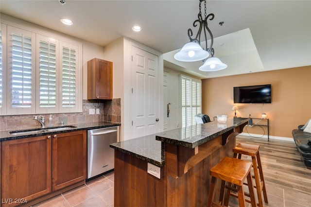 kitchen featuring dishwasher, hanging light fixtures, a breakfast bar area, sink, and a kitchen island