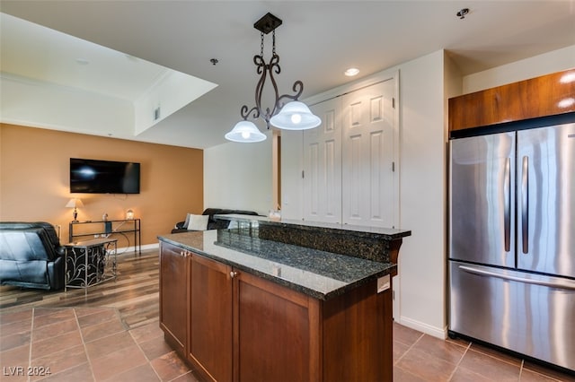 kitchen featuring stainless steel fridge, dark stone counters, dark tile patterned floors, a kitchen island, and decorative light fixtures