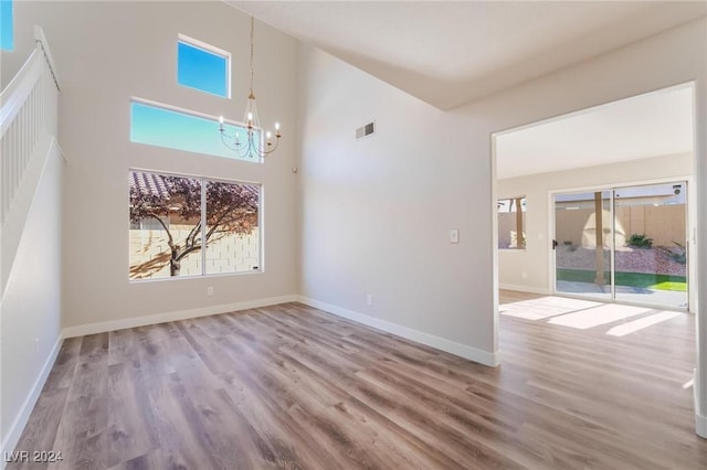 unfurnished room with hardwood / wood-style floors, a towering ceiling, and a notable chandelier