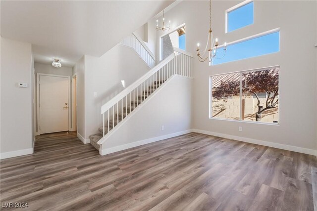 unfurnished living room with hardwood / wood-style floors, a healthy amount of sunlight, a towering ceiling, and an inviting chandelier