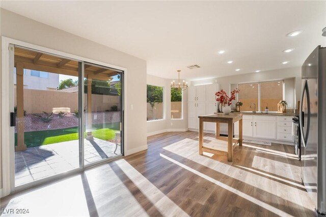 interior space with hanging light fixtures, a notable chandelier, white cabinetry, wood-type flooring, and stainless steel refrigerator