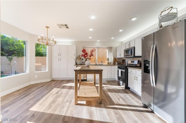 kitchen featuring white cabinets, light hardwood / wood-style floors, decorative light fixtures, and appliances with stainless steel finishes