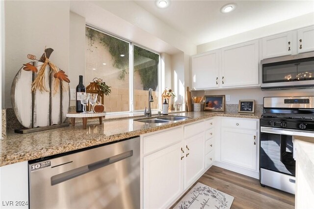 kitchen with hardwood / wood-style floors, white cabinets, sink, light stone countertops, and stainless steel appliances