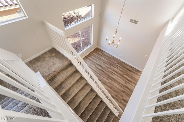 stairs with wood-type flooring and an inviting chandelier