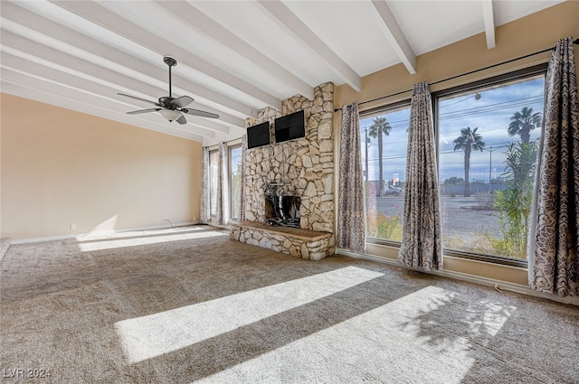 unfurnished living room featuring carpet flooring, beam ceiling, a stone fireplace, and ceiling fan