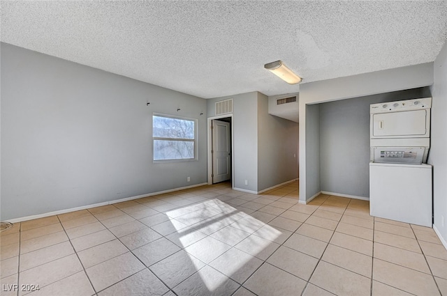 unfurnished bedroom with a textured ceiling, stacked washer and dryer, and light tile patterned flooring