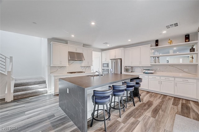 kitchen with white cabinetry, stainless steel appliances, a center island with sink, and light hardwood / wood-style flooring