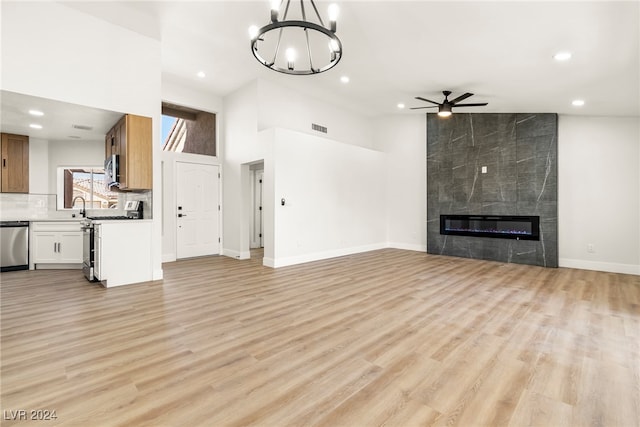 unfurnished living room featuring ceiling fan with notable chandelier, a towering ceiling, sink, a fireplace, and light hardwood / wood-style flooring