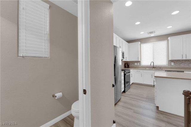 kitchen with backsplash, light hardwood / wood-style flooring, white cabinetry, and sink