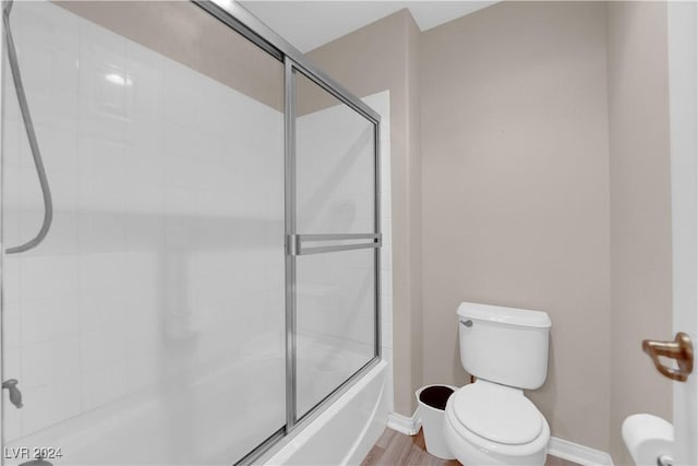 bathroom featuring hardwood / wood-style floors, combined bath / shower with glass door, and toilet