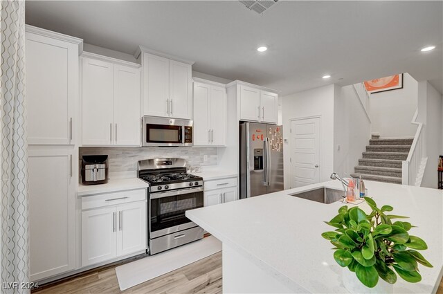 kitchen featuring white cabinetry, light wood-type flooring, stainless steel appliances, and decorative backsplash