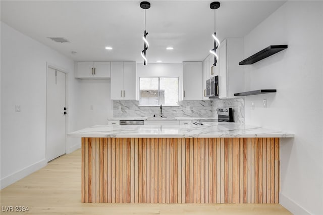 kitchen featuring stainless steel appliances, kitchen peninsula, white cabinetry, light hardwood / wood-style flooring, and decorative light fixtures