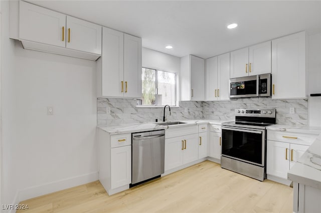 kitchen with light hardwood / wood-style floors, white cabinets, sink, light stone countertops, and appliances with stainless steel finishes