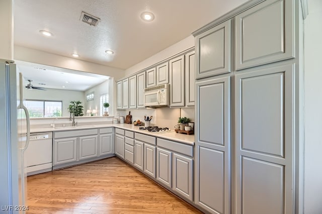 kitchen featuring sink, a textured ceiling, white appliances, light hardwood / wood-style flooring, and gray cabinetry