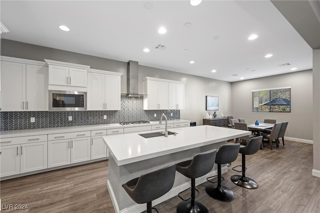 kitchen with wood-type flooring, a center island with sink, sink, and white cabinetry