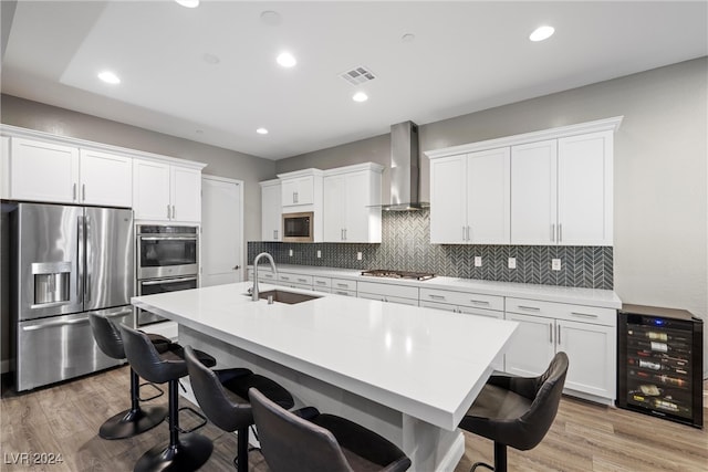 kitchen featuring sink, appliances with stainless steel finishes, wall chimney exhaust hood, beverage cooler, and white cabinets