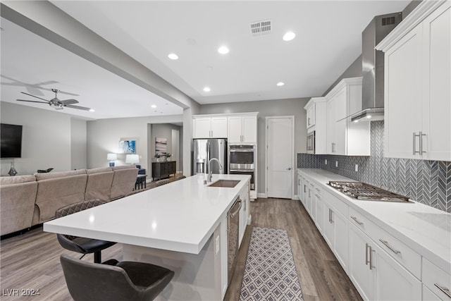 kitchen with wall chimney exhaust hood, hardwood / wood-style flooring, a kitchen breakfast bar, white cabinetry, and appliances with stainless steel finishes