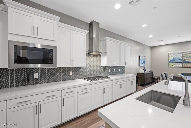 kitchen with stainless steel appliances, hardwood / wood-style floors, sink, wall chimney range hood, and white cabinetry