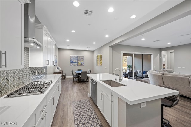 kitchen with stainless steel appliances, a center island with sink, wall chimney exhaust hood, sink, and white cabinetry