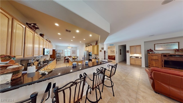 kitchen featuring dark stone counters, a chandelier, light brown cabinets, and kitchen peninsula