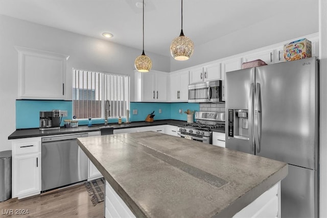 kitchen with stainless steel appliances, a center island, sink, white cabinetry, and decorative light fixtures