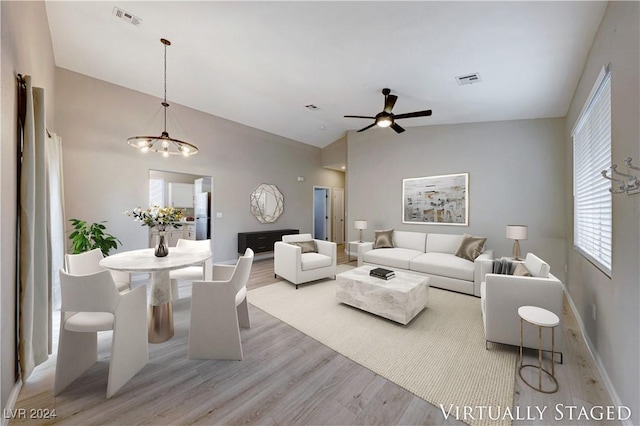 living room with ceiling fan with notable chandelier, vaulted ceiling, and light hardwood / wood-style flooring