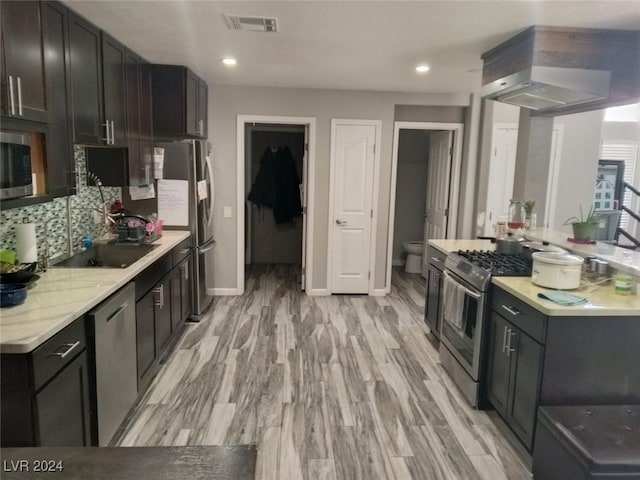 kitchen featuring decorative backsplash, light hardwood / wood-style floors, wall chimney range hood, and appliances with stainless steel finishes